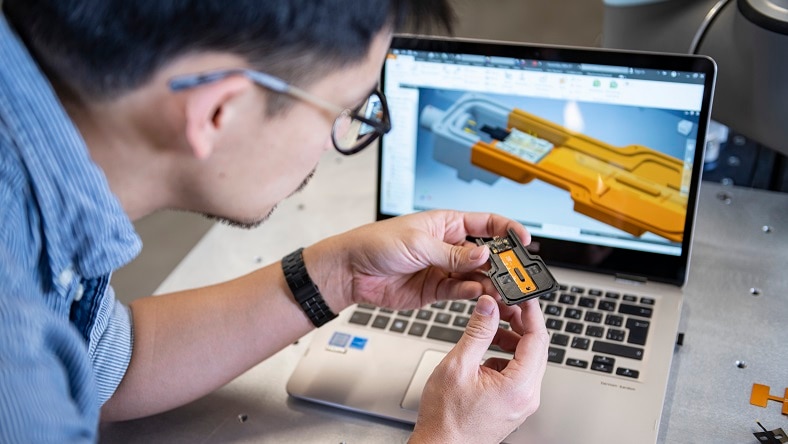 A man examines a manufactured part in front of computer-assisted design.